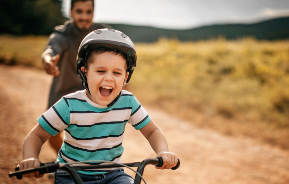 A young boy riding his bike outdoors with his dad